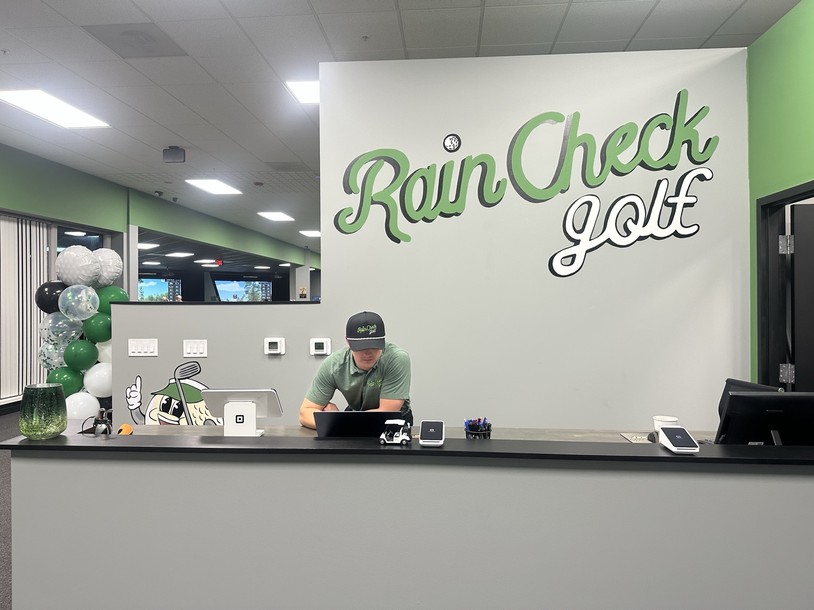 Front desk with the hand-painted Rain Check Golf logo wall