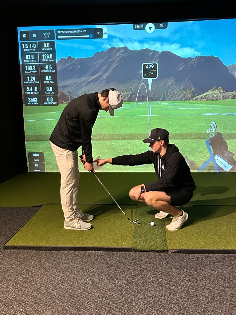 Golf lesson in progress - instructor coaching student at indoor simulator with Trackman data